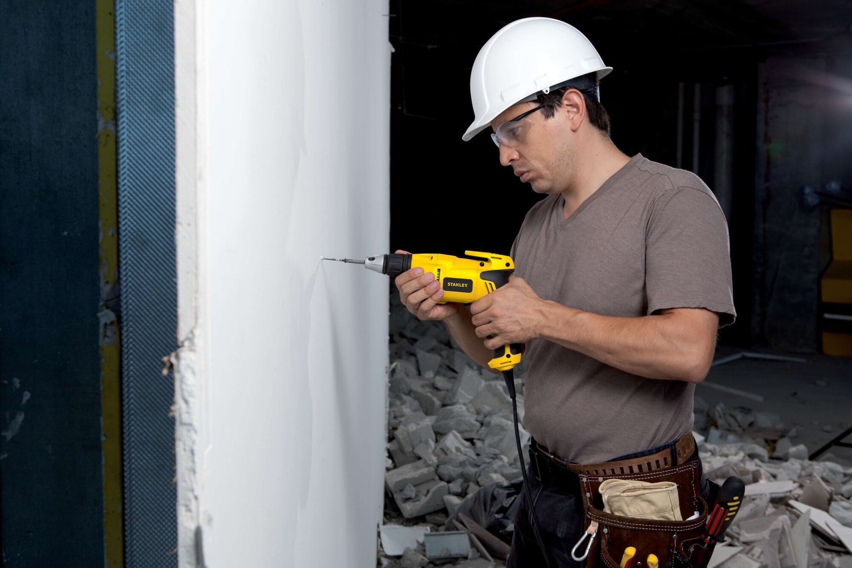 Stanley STDR5206 taladro con cable en panel de yeso, vista lateral, trabajador con equipo de seguridad.